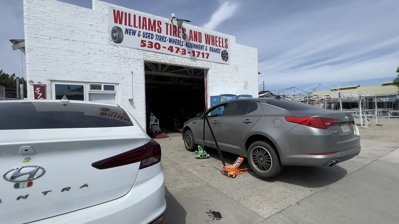 A customer's car up on jacks in front of the shop, under the Williams Tires And Wheels sign.